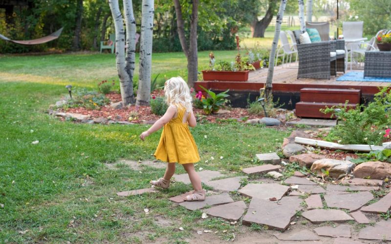 Cute young girl in yellow dress walking in the backyard on a summer day